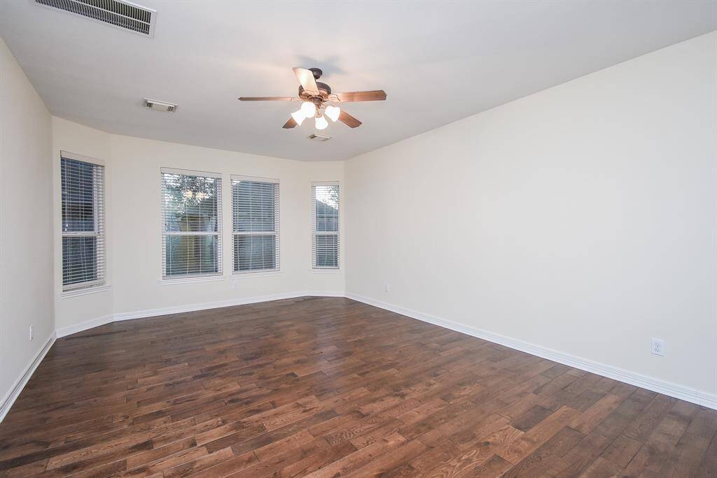 Primary bedroom with wood laminate flooring, ceiling fan & plenty of natural light from multiple windows.