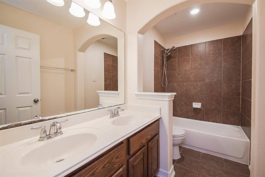 This bathroom features a double-sink vanity with a large mirror, warm wood cabinetry, and a well-lit space.