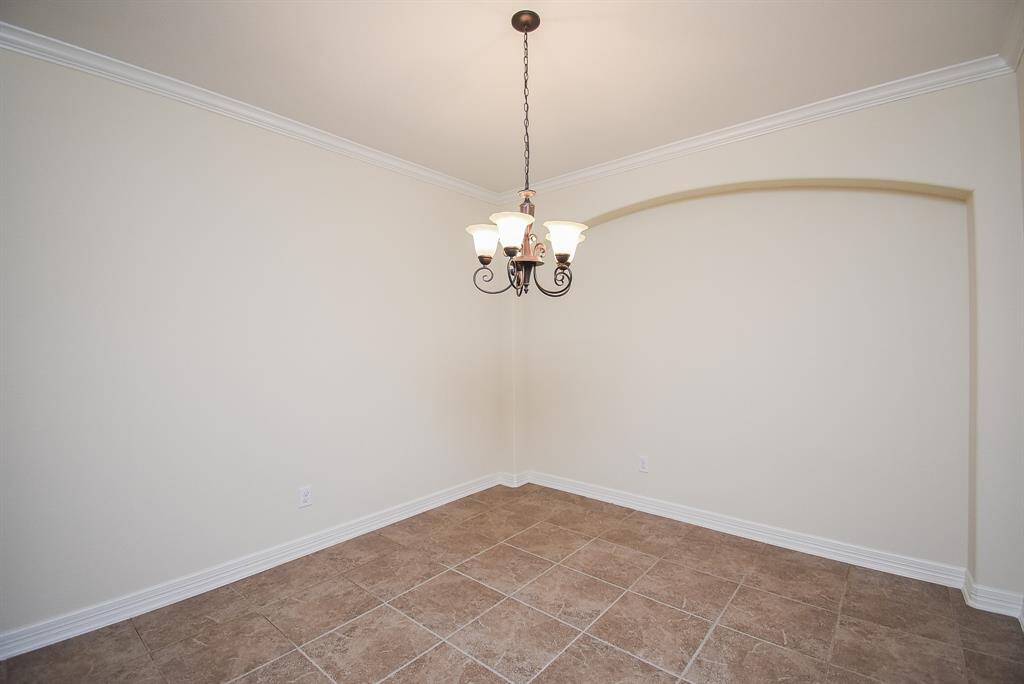 The formal dinning room offers neutral walls, tiled flooring, a decorative chandelier and an arched niche to add architectural interest.