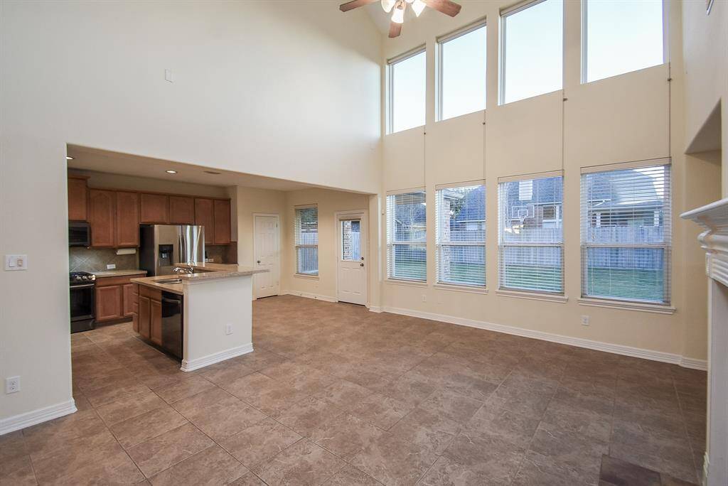 Spacious living area with high ceilings and ample natural light from large windows. Open concept connects to a modern kitchen with stainless steel appliances and wooden cabinetry.