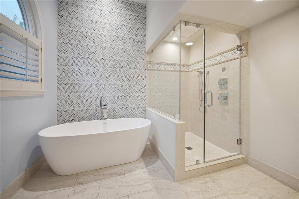 The Primary Bath has shutters to control western light.  Beautiful tile wall behind Tub and accent in shower area.  High ceiling with an art light and full glass enclosure.