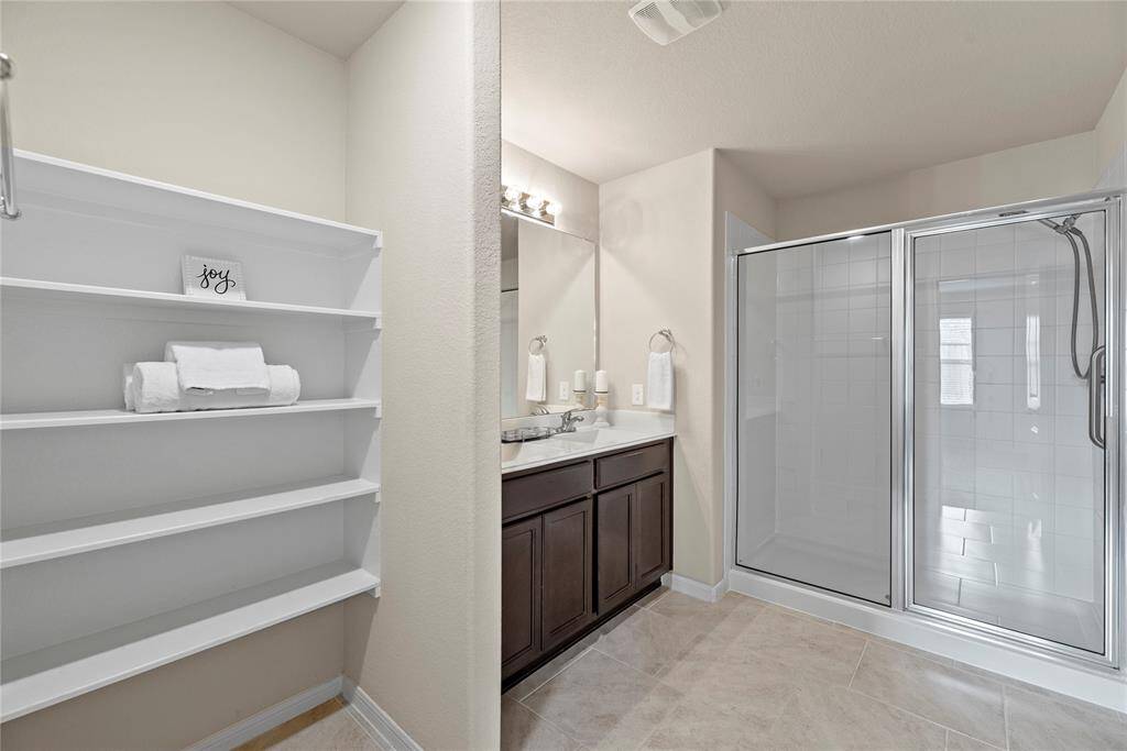 The expansive walk-in shower, adorned with stunning tile work and a sleek glass front, offers a luxurious escape for a quick rinse or a refreshing retreat. The additonal built-in shelving ensures a place for everything.
