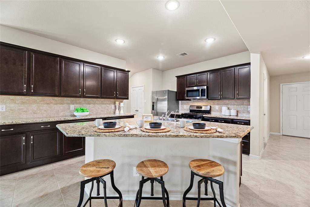 Your chef inspired kitchen awaits! Features include granite countertops paired with a coordinating stone backsplash, stainless steel appliances, rich cabinets with updated hardware, under cabinet lighting, recessed lighting, and a sprawling island with breakfast bar seating.