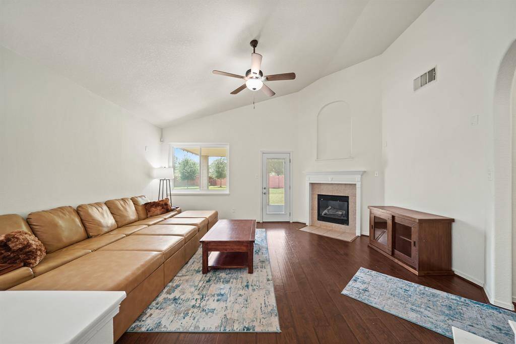 The living room sits on the back of the home with a high ceiling, ceiling fan with light fixture & laminate hardwood floors.