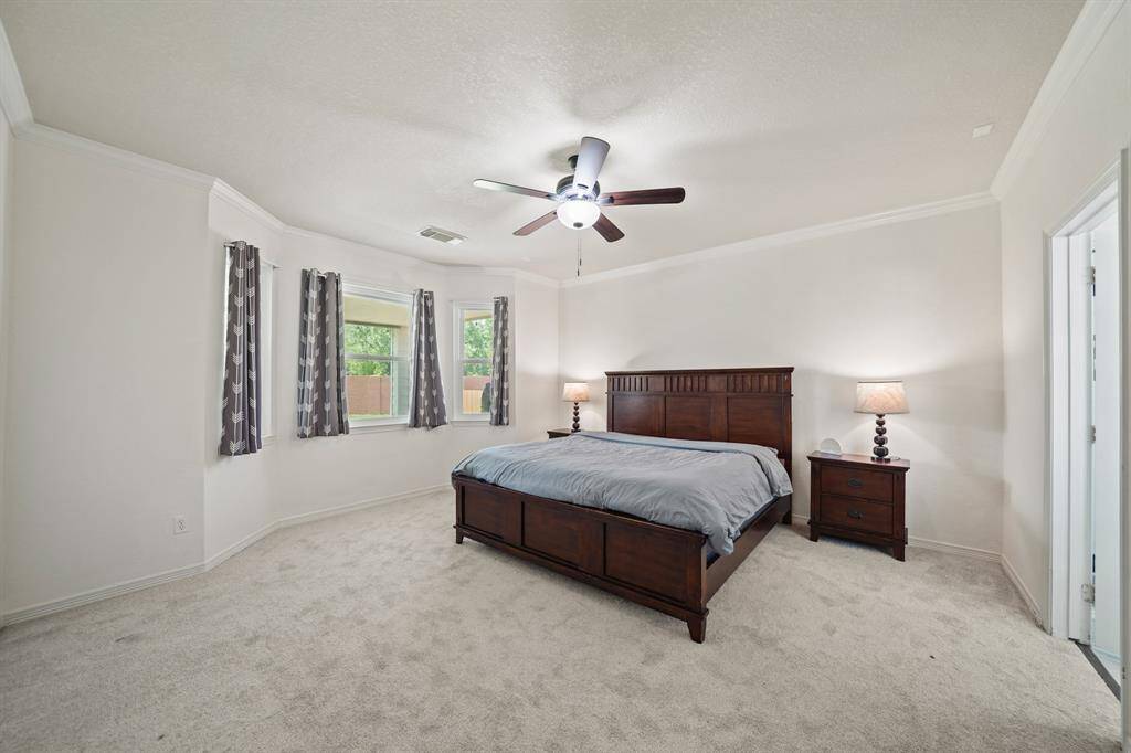 The private owner's suite situated on the back of the home with a bay of windows with drapes overlooking the backyard includes crown moulding, ceiling fan with lighting, pre-wiring or ceiling speakers & carpet.