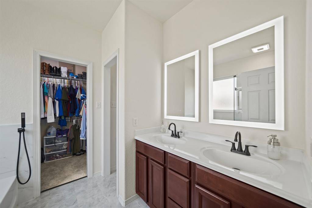 The private bath includes wood-stained cabinets supporting a solid surface counter top with integrated dual sinks & back splash highlighted by lighted mirrors & tile flooring.