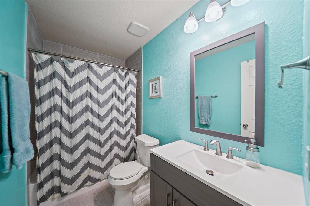 Remodeled in 2023 and serving as the home's second full bath, features include a Shaker-style cabinet supporting a solid surface counter top with integrated counter top & sink accompanied by a framed mirror with lighting above. Included is a tub-to-ceiling ceramic tile surrounded combination tub/shower and tile flooring.