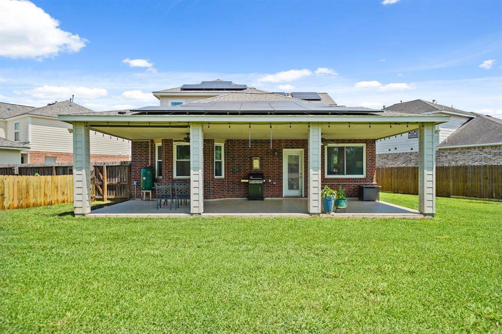 A view of the back of the home and covered patio. A large side yard is shown on the right with gated access to the front of the home.