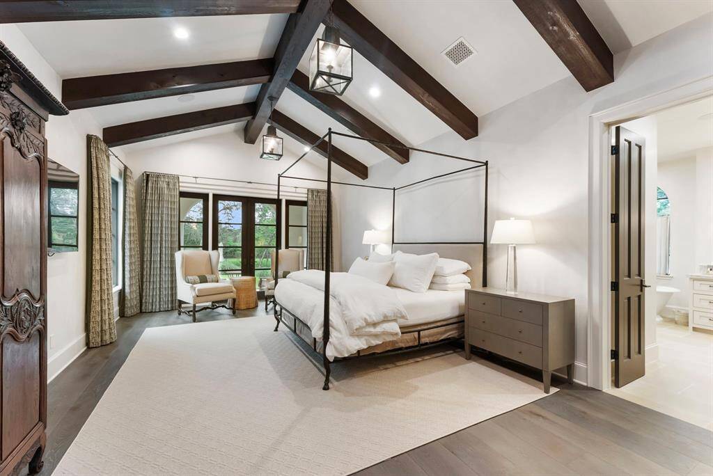 The private primary bedroom retreat features wood flooring, a vaulted ceiling with exposed wood beams, and direct access to a secluded patio.