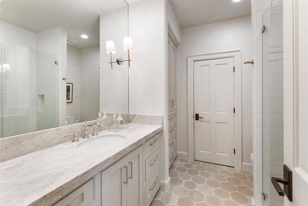 Luxurious en-suite bathroom with stone flooring, leathered quartzite countertop, custom cabinetry and a tiled walk-in shower.