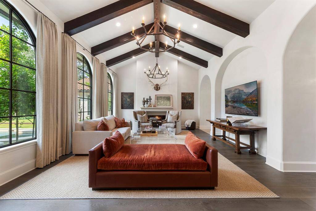 The family room is a true showstopper, featuring rich wood flooring, a soaring vaulted ceiling with antique wood beams, and stunning arched windows that frame picturesque views of the backyard.