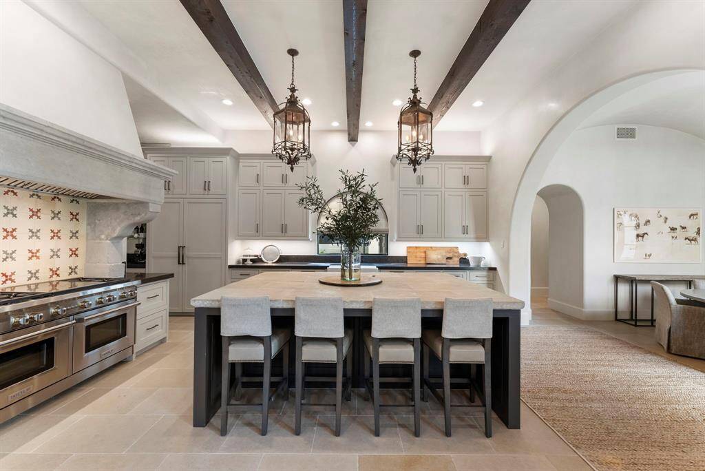 A culinary masterpiece, the kitchen boasts a reclaimed limestone island, luxurious Belgian bluestone countertops, designer lighting, and architectural wood beams and arches that echo the home’s timeless style.