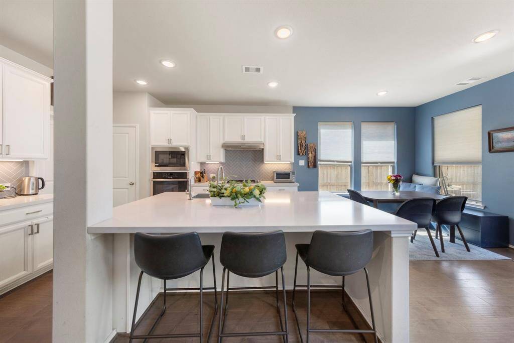 The clean and bright kitchen boasts an extended upgraded island with seating, sleek white cabinetry, and contemporary fixtures.