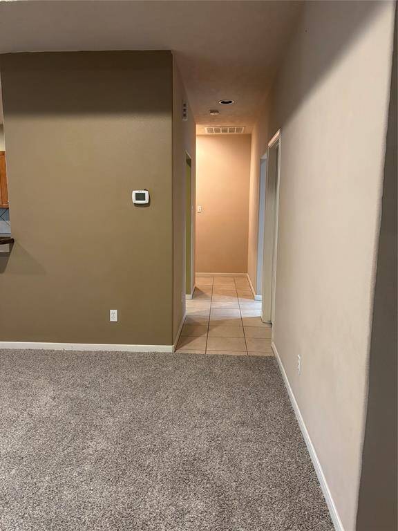 The photo shows a hallway with a mix of carpet and tile flooring. The walls are painted in neutral tones. The space leads to additional rooms.