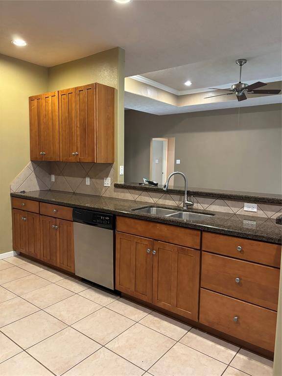 Modern kitchen with ample wooden cabinets and granite countertops. Includes a double sink, stainless steel dishwasher, and tiled backsplash. Open layout with adjacent living space, ceiling fan, and recessed lighting.
