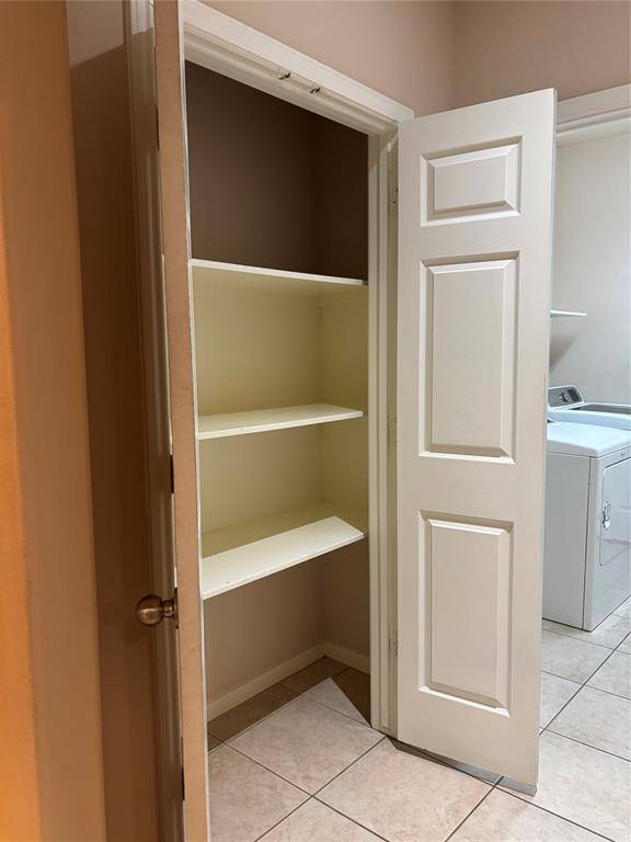 Storage closet with white shelves, ideal for storage. It's located next to a laundry area with a washing machine, both set on tiled flooring.