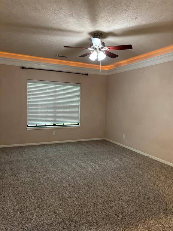 Primary bedroom with neutral walls, a plush carpet, and a ceiling fan with lights. It has a window with blinds and crown molding with recessed lighting, creating a cozy atmosphere.