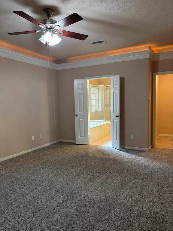 This spacious Primary bedroom features a ceiling fan, carpeted flooring, and crown molding with accent lighting. Double doors open to a bright en-suite bathroom with a bathtub.