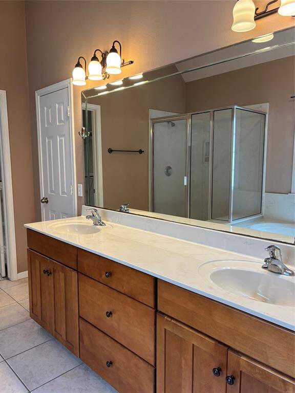 This bathroom features a spacious double vanity with ample storage, a large mirror, modern light fixtures, and a glass-enclosed shower.