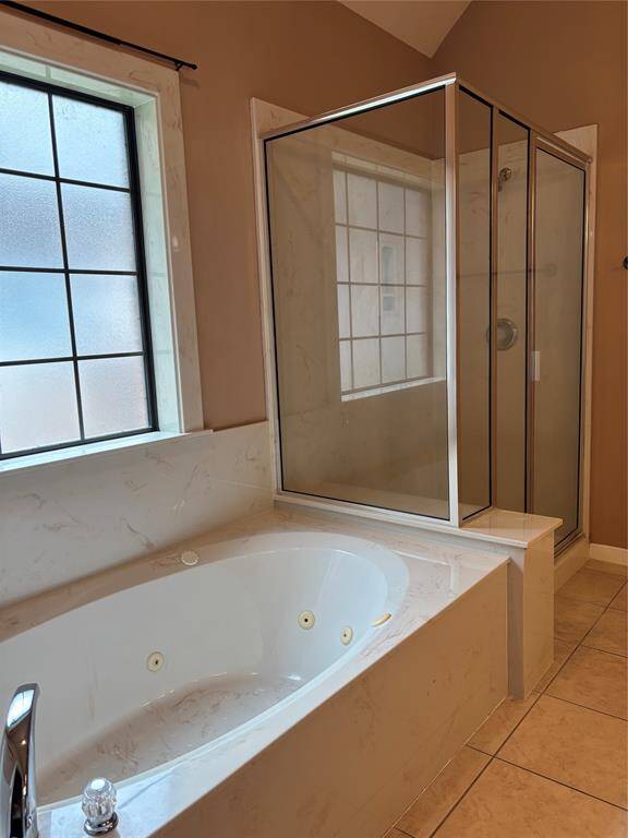 This bathroom features a luxurious corner jetted bathtub with a marble surround, next to a spacious glass-enclosed shower. Natural light streams through the frosted window, enhancing the warm, inviting atmosphere.