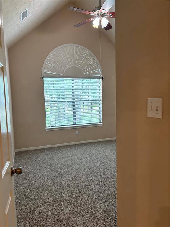 This room features a vaulted ceiling with a ceiling fan, a large arched window with blinds, neutral wall colors, and carpeted flooring, offering a cozy and inviting space.