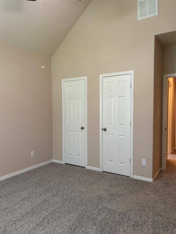 This room features neutral walls, a vaulted ceiling, and carpeted flooring. It includes two white doors, for closets, offering ample storage space. The room has a simple and clean design, with a visible hallway entrance.