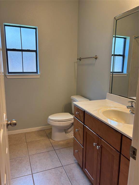 Secondary bathroom featuring, a modern design with neutral tones. It includes a tiled floor, a toilet, a wooden vanity with a sink, a large mirror, and a window for natural light.