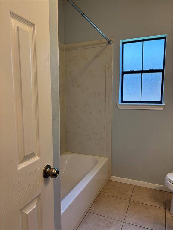 Secondary cozy bathroom featuring a bathtub with a shower rod, tiled flooring, and a frosted window for privacy.