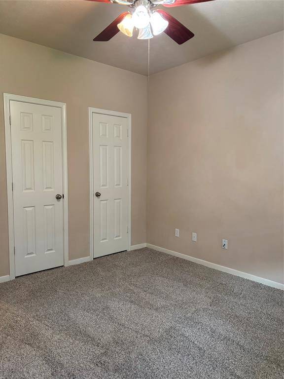This room features neutral walls, carpeted flooring, a ceiling fan with lights, and two white doors, for closet space.