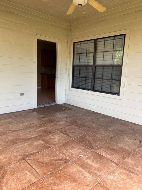 This is a covered patio with tiled flooring, a ceiling fan, and a doorway leading to the interior. It offers a cozy space for outdoor relaxation.