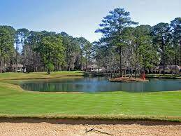 This photo showcases a scenic view of a golf course with a pond, well-maintained greens, and lush trees, offering a tranquil and picturesque setting.