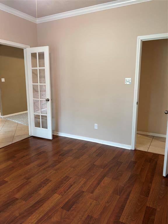 This room features warm wood flooring, neutral beige walls, and white trim. It includes a doorway with glass-paneled French doors leading to a tiled area, providing a bright and open feel.
