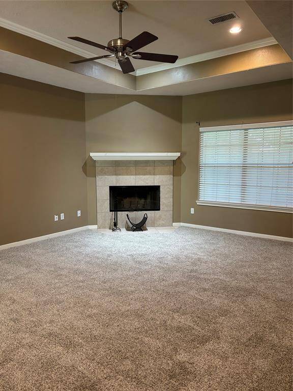 This inviting living room features a cozy fireplace, neutral walls, plush carpeting, and a ceiling fan. The large window lets in natural light, creating a warm and welcoming atmosphere.