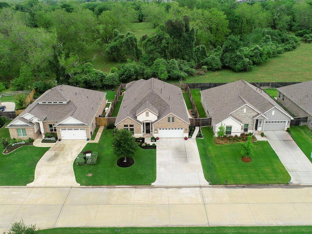 This aerial view showcases the home’s excellent curb appeal. It also shows off the extended driveway, providing additional space for parking, drawing with sidewalk chalk, and a neighborhood basketball game. Notice the open greenery located behind the house’s fence line, untouched and natural.
