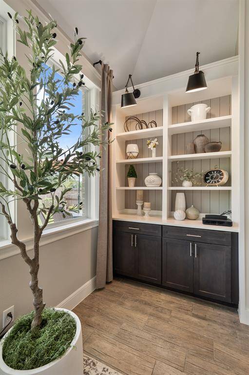 These built-in bookshelves are located to the left of the fireplace and add function and style to the space. Museum lighting shines down, illuminating the shiplap backing, quartz countertop, and stained wood cabinetry. The closed storage below provides a place for gaming equipment and consoles while the open storage above is ideal for displaying family mementos.