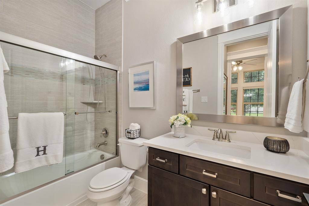 This Secondary Bathroom is accessible from both the Foyer and previously seen Secondary Bedroom. The space includes an undermount sink, quartz countertop, stained-wood cabinets, framed mirror, and shower/tub combo with tile that washes all the way up to the ceiling.
