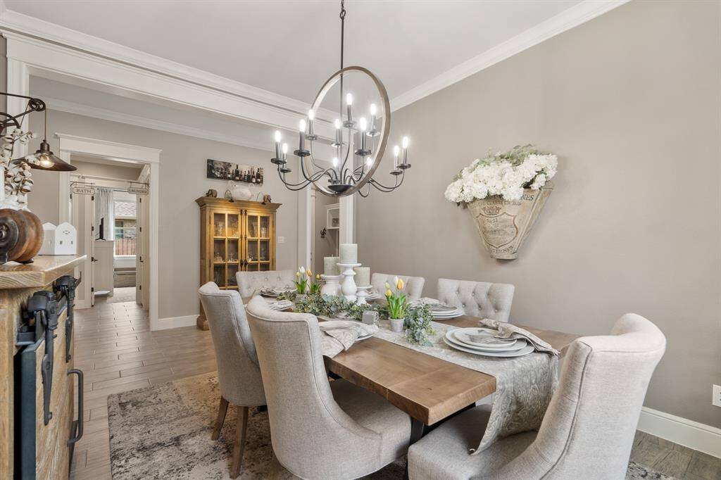 The charm is in all the fine finishes and attention to detail. Notice how the designer wood and iron chandelier coordinates with the flooring, color palette, and nearby furniture. This angle also highlights the cased opening between the Foyer and Dining Room, in addition to the Secondary Bedroom hallway ahead.