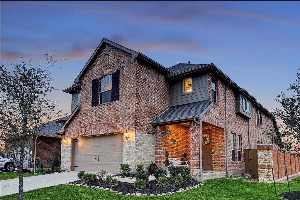 Charming brick home with a welcoming front porch, beautifully landscaped yard, and elegant evening lighting.