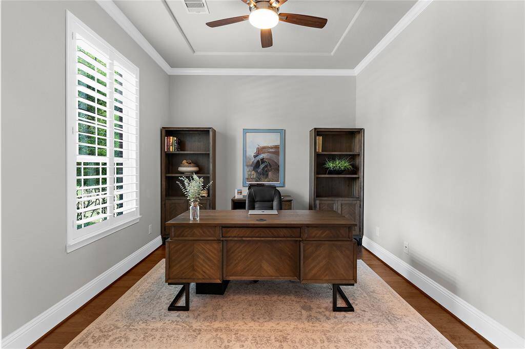 This snazzy home office displays plantation shutters, vaulted ceilings with fan and wood flooring.