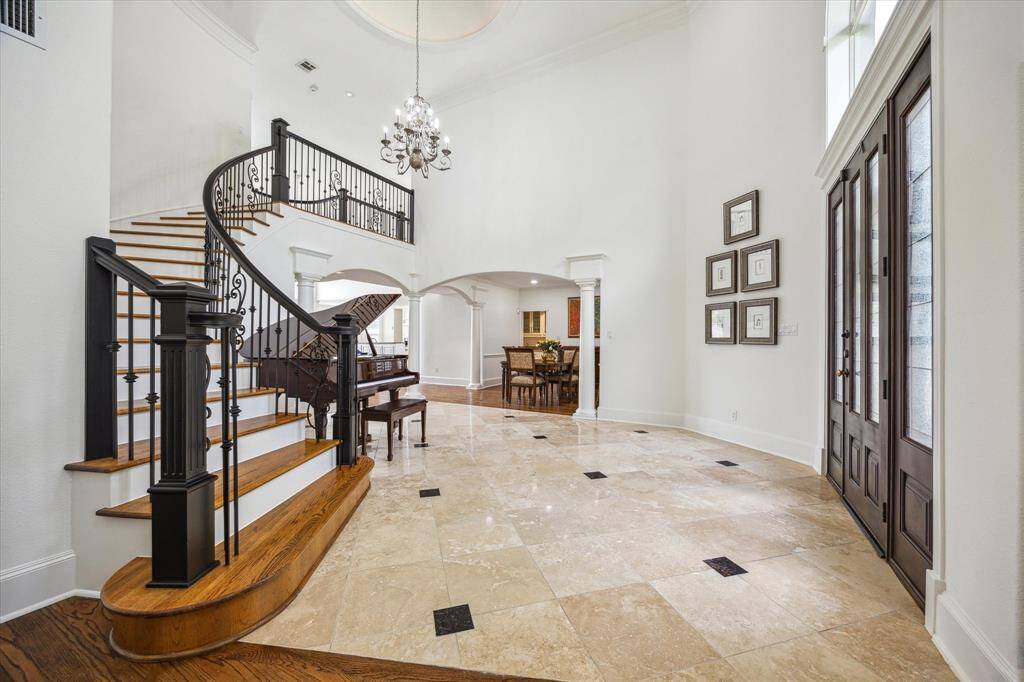 Two story entry with travertine flooring and elegant curved staircase with painted wood banister and wrought iron railing.