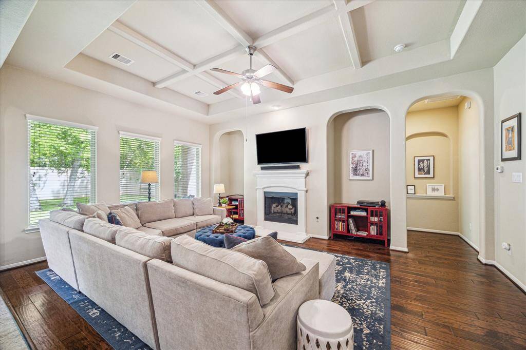 This lovely family room is the perfect place to gather with friends and family or enjoy a quiet, peaceful evening at home with your favorite person. A wall of windows fills the space with natural light, highlighting the warm wood flooring, soft neutral paint, and elegant coffered ceiling above. A romantic gas-log fireplace anchors the room, creating a cozy yet spacious atmosphere designed for both everyday comfort and effortless entertaining.