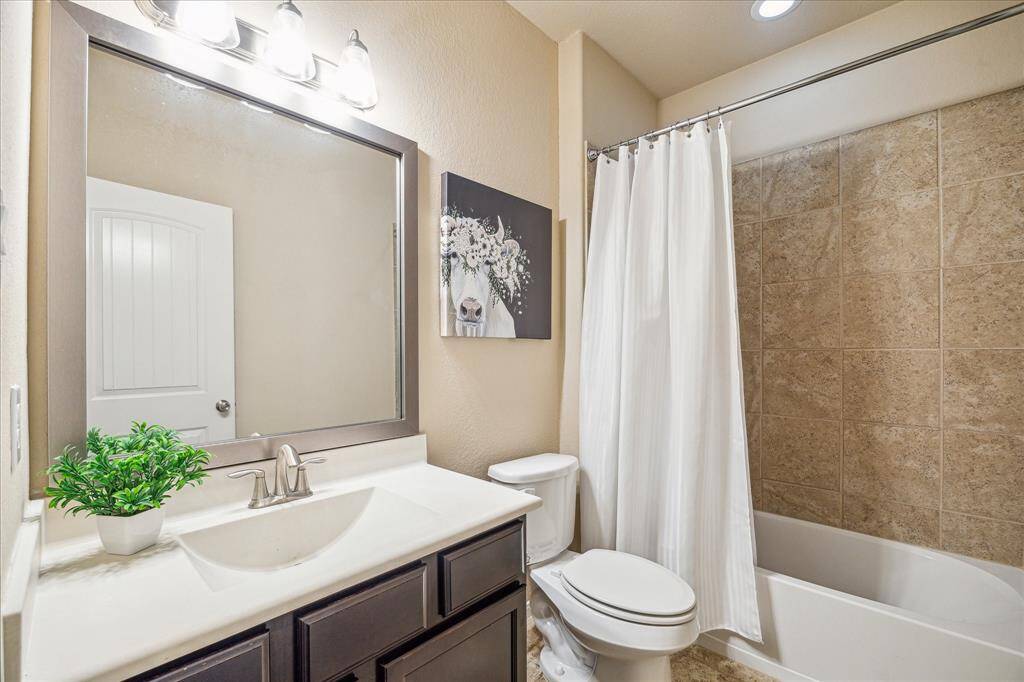 This full bathroom offers both style and convenience, with a single sink vanity topped by a framed mirror and elegant lighting, plus a convenient tub/shower enclosure perfect for daily use.