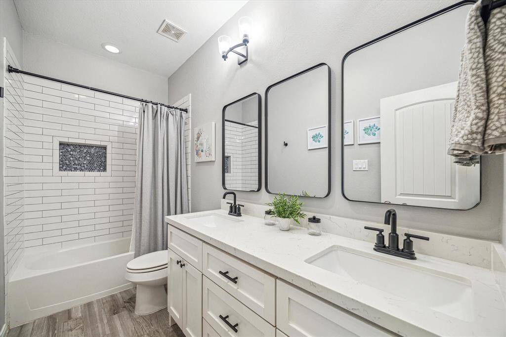 This updated guest bathroom is as functional as it is stylish, with an extended dual sink vanity, chic mirrors with stylish lighting, and updated tile in the tub/shower enclosure.