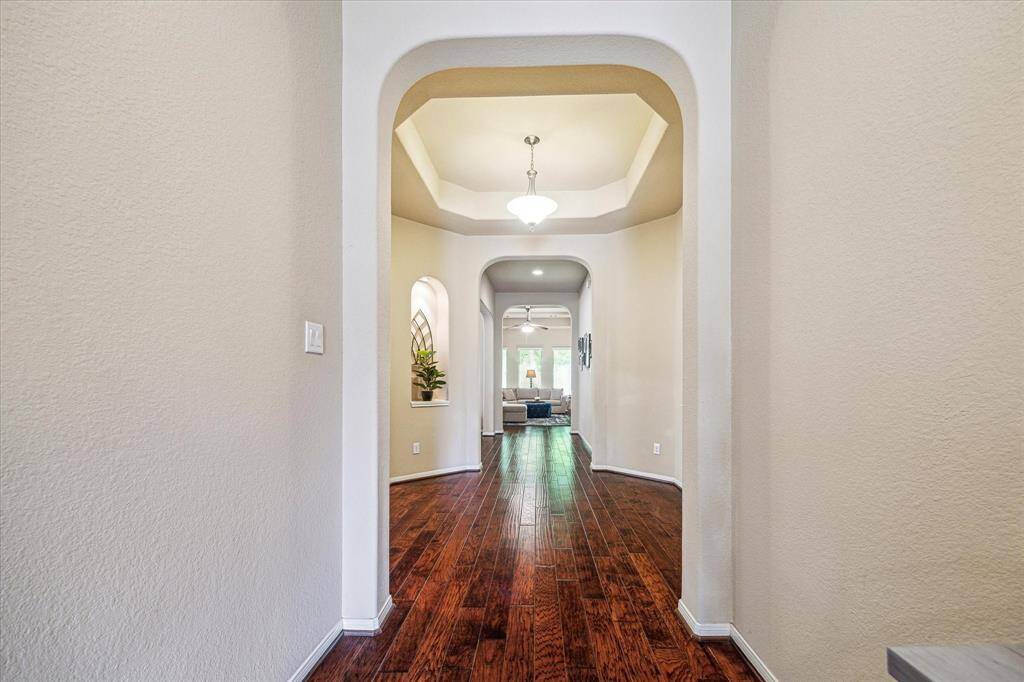 Step inside to discover elegant finishes from the front door to the back. Find gorgeous wood flooring, neutral paint, lit art niches, striking raised tray and coffered ceilings, elegant lighting and fans, and previews of the family room directly ahead.