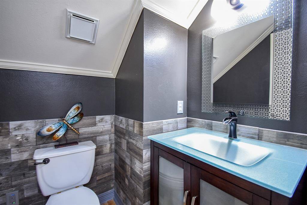 Custom updated powder bath with tile wainscot, new vanity with glass vanity top, updated fixture and ornate vanity mirror.