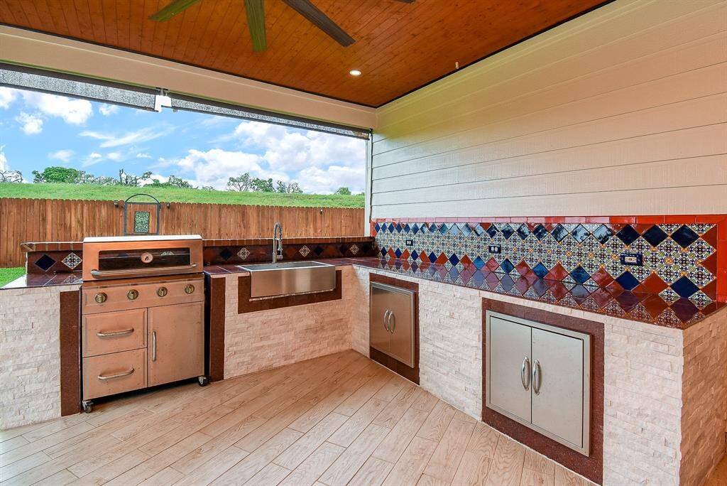Dedicated area for gas grill, stainless steel farmers’ sink, granite counters and custom tile backsplash. The gas grill can be rolled away from the wall for easy clean-up and maintenance. Stacked stone adorns the cabinet surround.
