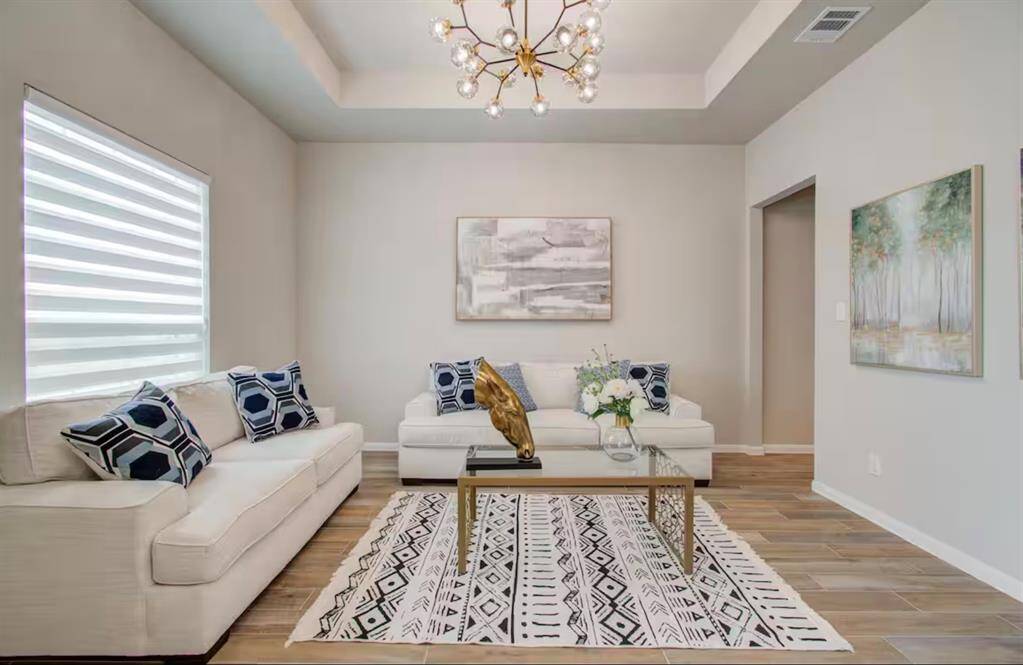The den features beautiful floors, high tray ceilings, chandelier, and large window.