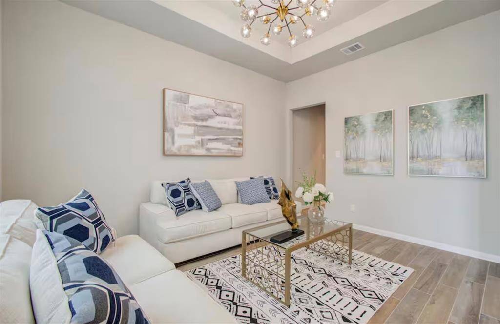 The den features beautiful floors, high tray ceilings, chandelier, and large window.