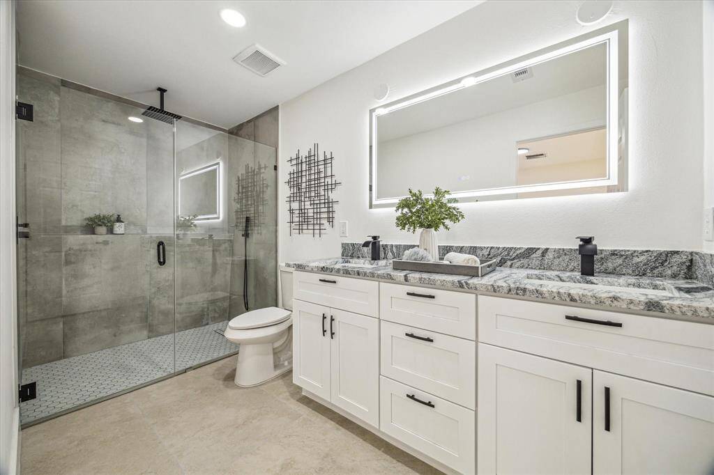 Modern and refined, the en-suite bath boasts a frameless glass shower, double sinks, and striking black and white granite countertops.