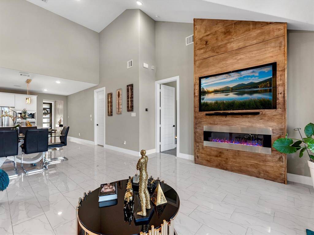 The room boast an open layout  connecting the  living room and dining areas for spacious feel, the soft neutral paint colors making the room feel modern  and versatile. Encasing a focal point a built in beautiful accent wall wall to display the tv and elegant modern electric chimney wit a built in surround system for the family to enjoy creating lifestyle memories!